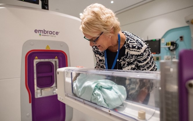 A female doctor looking over a baby about to enter the NICU MRI system.