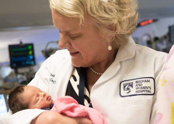 A female doctor holds a newborn baby in the Brigham and Women's Hospital Newborn Intensive Care Unit.